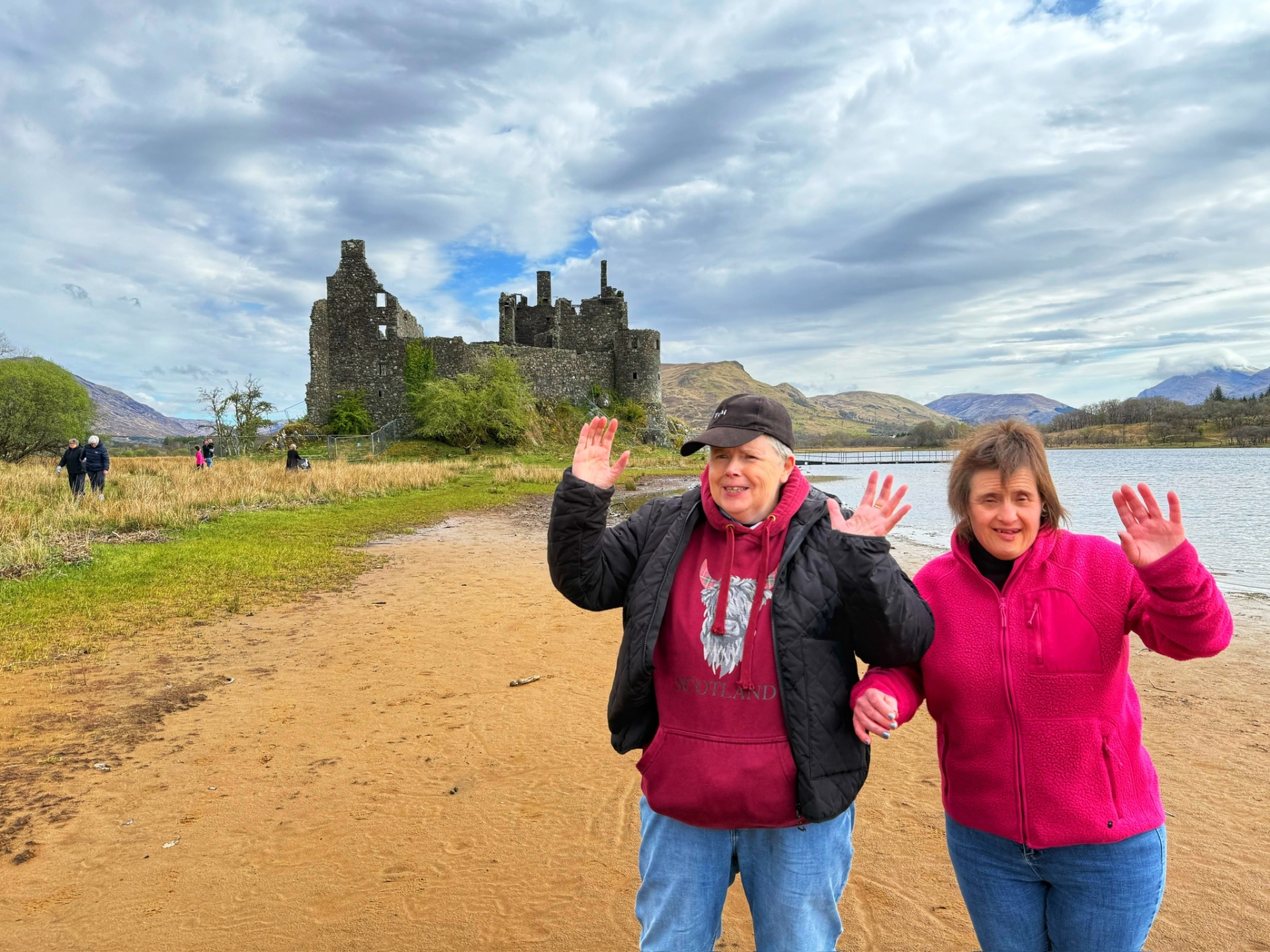 Residents waving in front of a Scottish castle and loch