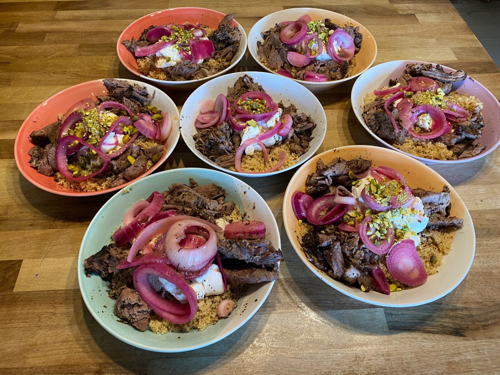 Bowls of couscous with meat, yoghurt and pickled onions