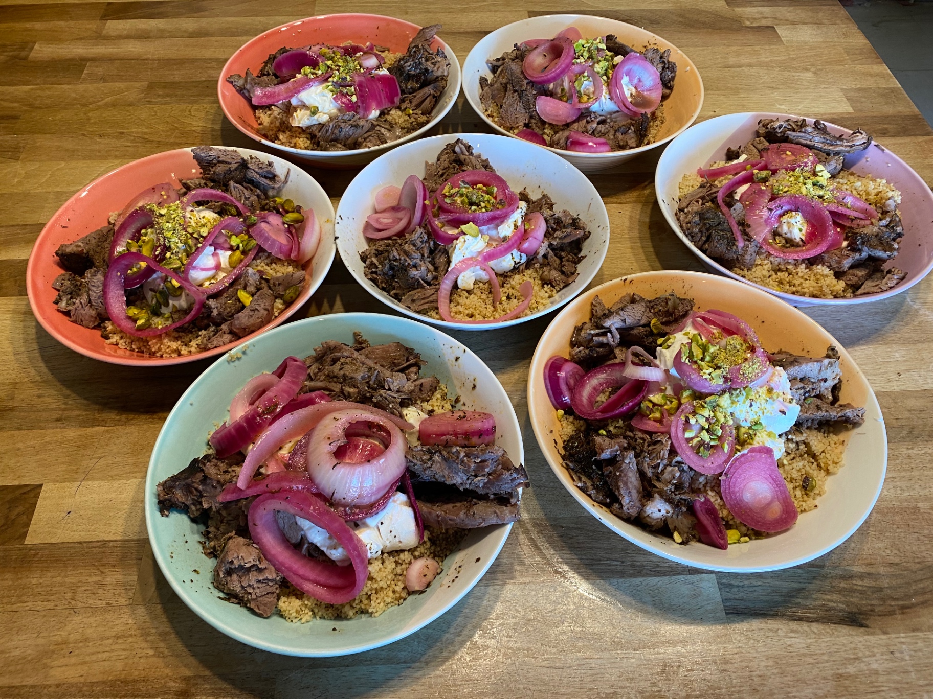 Bowls of couscous with meat, yoghurt and pickled onions